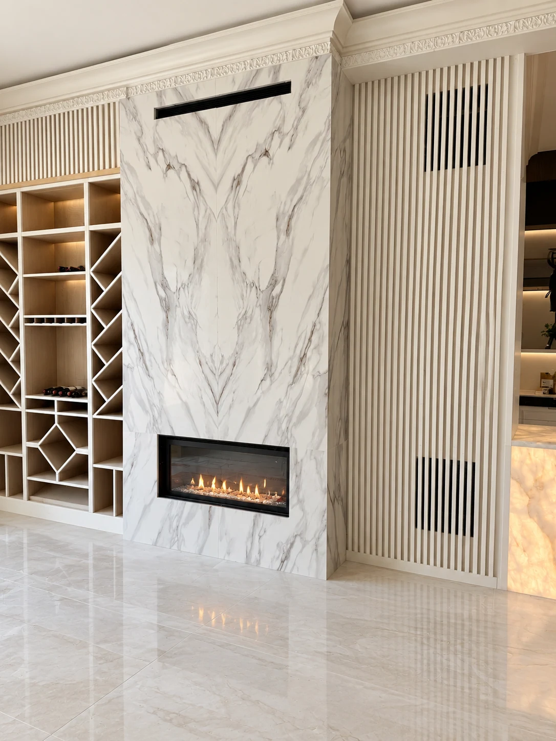 Tall white and gray stone fireplace surround beside wine shelving; retouched setting, stone color and veining preserved